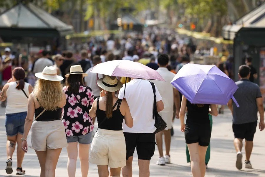 Un grupo de turistas se protege del sol con sombrillas este domingo en Barcelona.